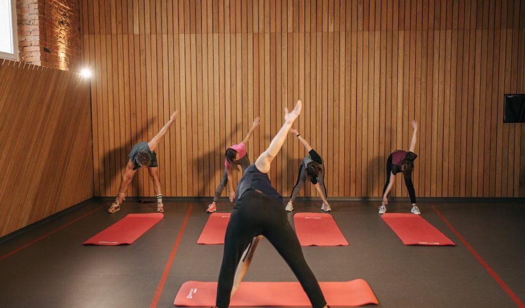 Yoga class with diverse adults stretching on mats in a cozy wooden studio.
