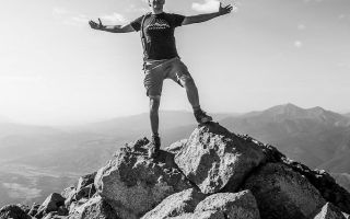 man in black tank top and white shorts standing on rock formation during daytime