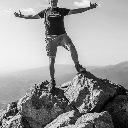 man in black tank top and white shorts standing on rock formation during daytime