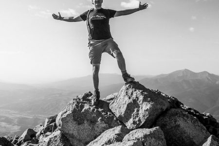 man in black tank top and white shorts standing on rock formation during daytime